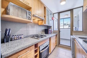 A modern kitchen with granite countertops, wooden cabinets, a built-in oven, a gas stove, and a toaster. - Angamos Coast Luminous Apartment 3D in Reñaca (Viña del Mar)