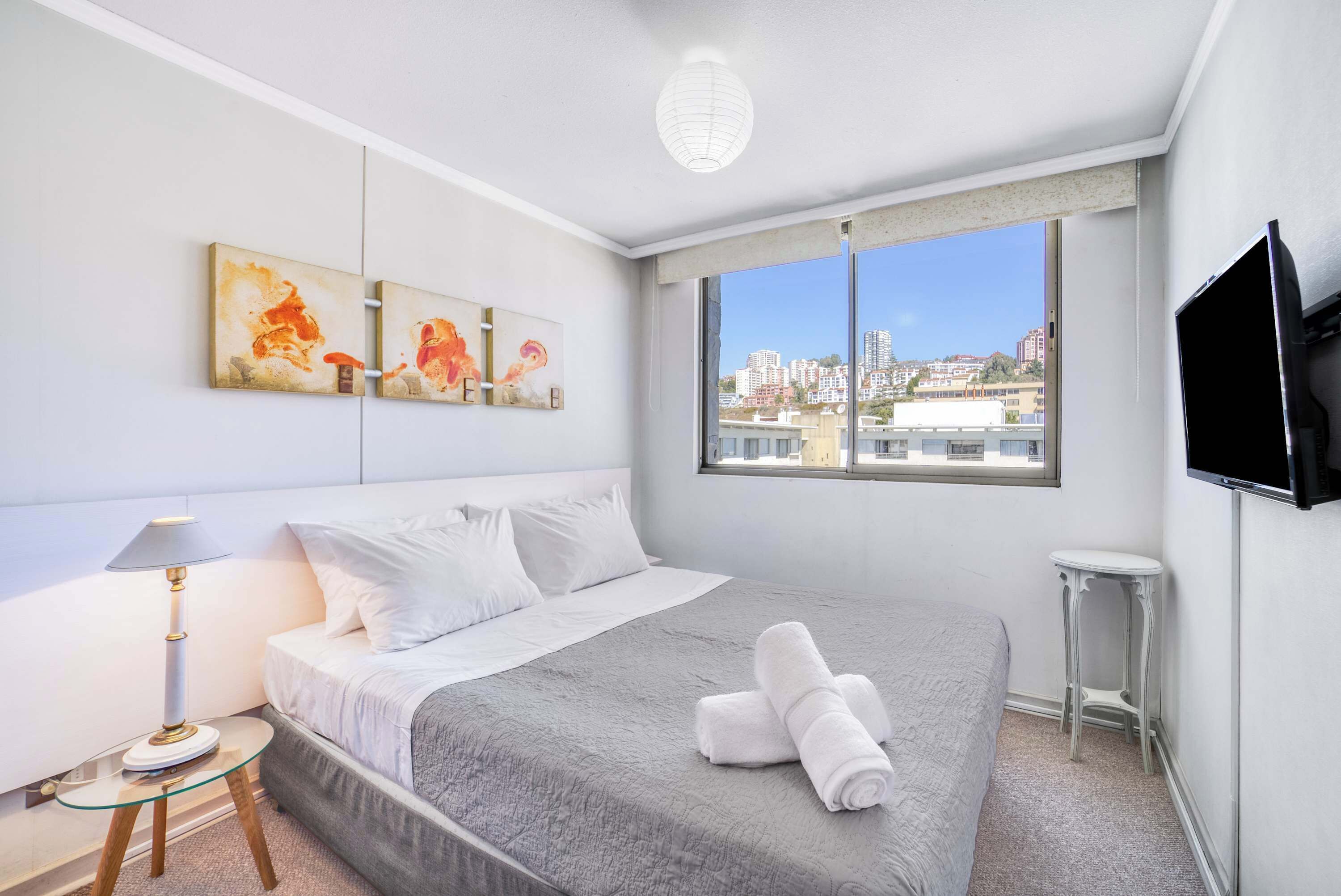 Habitación de hotel con cama, televisor, obras de arte en la pared y ventana con vista a la ciudad.