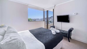 Ett hotellrum med en säng, en TV, en sittgrupp och ett stort fönster med utsikt över staden.