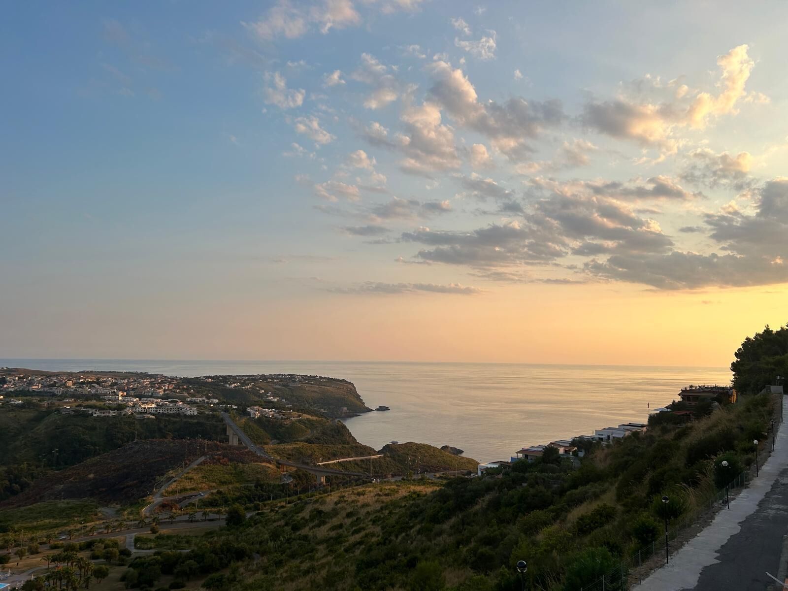 A coastal landscape with a bridge, a road, and buildings along the hillside.