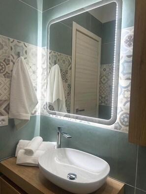 Ein Badezimmer mit einem weißen Waschbecken, einem Spiegel mit LED-Beleuchtung und Wandfliesen mit Muster.