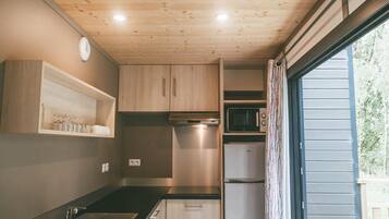 Une cuisine de taille réduite, dotée de meubles en bois, d’un four à micro-ondes, d’un réfrigérateur et d’une fenêtre avec des rideaux.