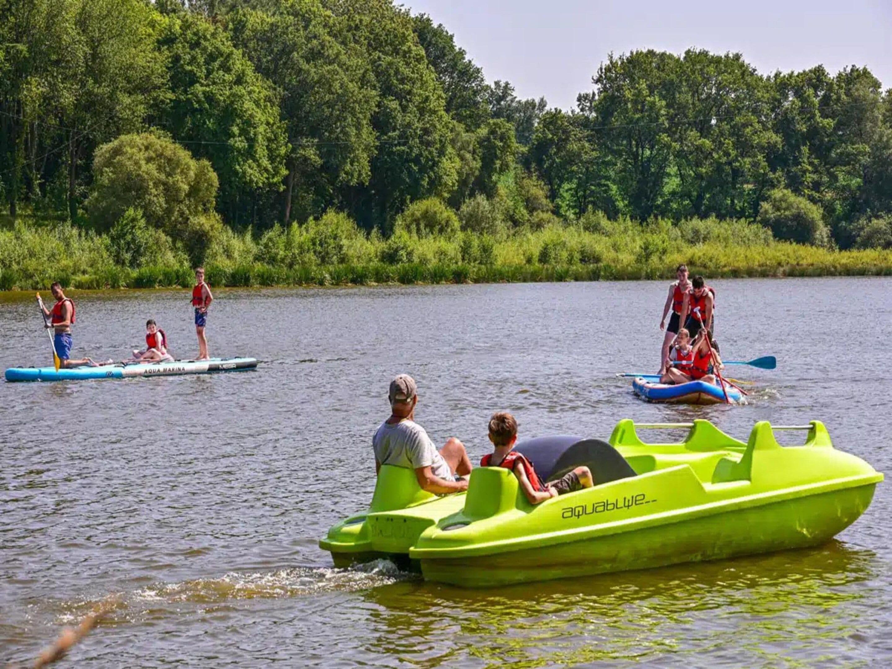 Mensen maken een tochtje op waterfietsen op een kalm meer, omringd door groen.