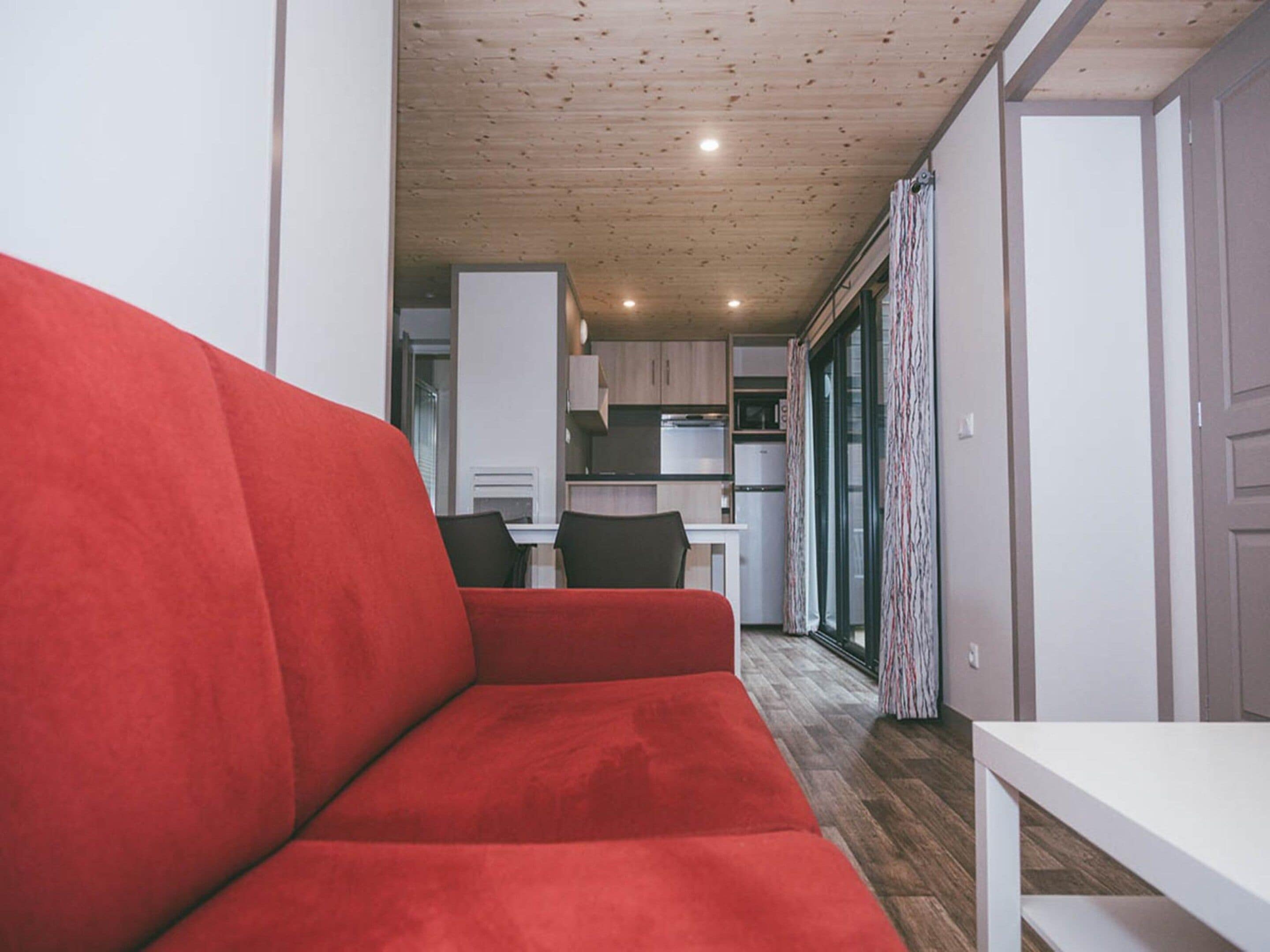 Un espacio habitable compacto con un sofá rojo, una zona de comedor y una kitchenette.