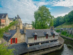 A riverside building with a stone facade and red shutters, adjacent to a larger stone structure with a tower. - 2-bedroom Family Chalet in Malansac (Malansac)