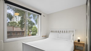 Une chambre avec une grande fenêtre, un lit, une table de chevet avec une lampe et une prise électrique.
