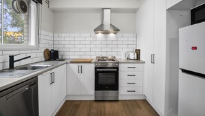 Une cuisine moderne avec des armoires blanches, une cuisinière en acier inoxydable, un four encastré et une fenêtre avec une grille d’aération.