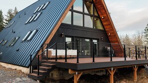 Un bâtiment moderne doté d’un toit en pente, de grandes fenêtres et d’une terrasse avec des sièges extérieurs.