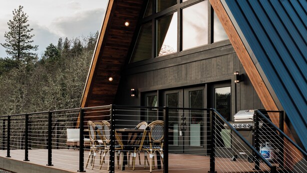 Une maison moderne dotée d’une terrasse en bois, d’un barbecue et d’un escalier menant à l’entrée.