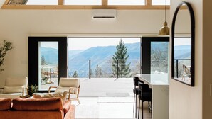 Un intérieur moderne comprenant un canapé, des fauteuils, un coin repas et une grande fenêtre donnant sur une vue imprenable sur les montagnes.