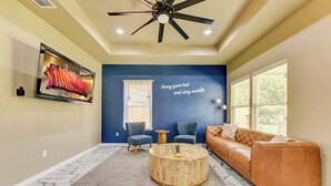 A living room with a blue accent wall, a ceiling fan, a mounted meat display, a round wooden coffee table, a leather sofa, and a marble-patterned floor. - Gem On Pearl w/ Pool - Walk to Downtown Lockhart (Lockhart)