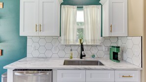 A kitchen with white cabinets, a sink, a dishwasher, a window with curtains, and a coffee maker. - Gem On Pearl w/ Pool - Walk to Downtown Lockhart (Lockhart)