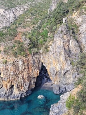 A rocky coastal landscape with a narrow passage leading to a clear blue water body. - STILL HOUSE 1908 (Atrigna)