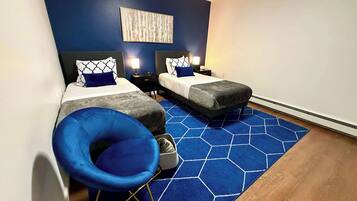 Une chambre d’hôtel avec deux lits, une chaise bleue, un tapis bleu en forme d’hexagone et une œuvre d’art murale.