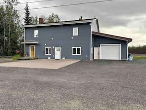 A two-story house with a garage, a front porch, and a driveway. - Modern Ground-Level Suite | King Bed, Near Airport (Fairbanks)