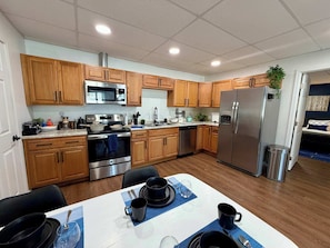 A modern kitchen with wooden cabinets, stainless steel appliances, and a dining area with a table set for two. - Modern Ground-Level Suite | King Bed, Near Airport (Fairbanks)