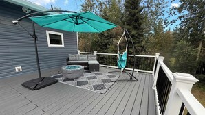 Eine Terrasse mit einer grauen Couch, einer runden Feuerstelle und einem Hängesessel.