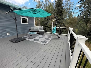 A deck with a gray sofa, a round fire pit, and a hanging chair. - Modern Spacious 5bd King Bed, Deck, Near Airport (Fairbanks)