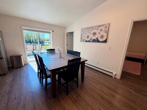 Een eetruimte met een houten tafel en stoelen, een schilderij aan de muur en een schuifdeur die leidt naar een terras.
