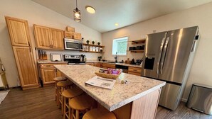 Eine moderne Küche mit Holzausstattung, einer Arbeitsplatte aus Granit, Edelstahlgeräten und einer Bar mit Sitzgelegenheiten.