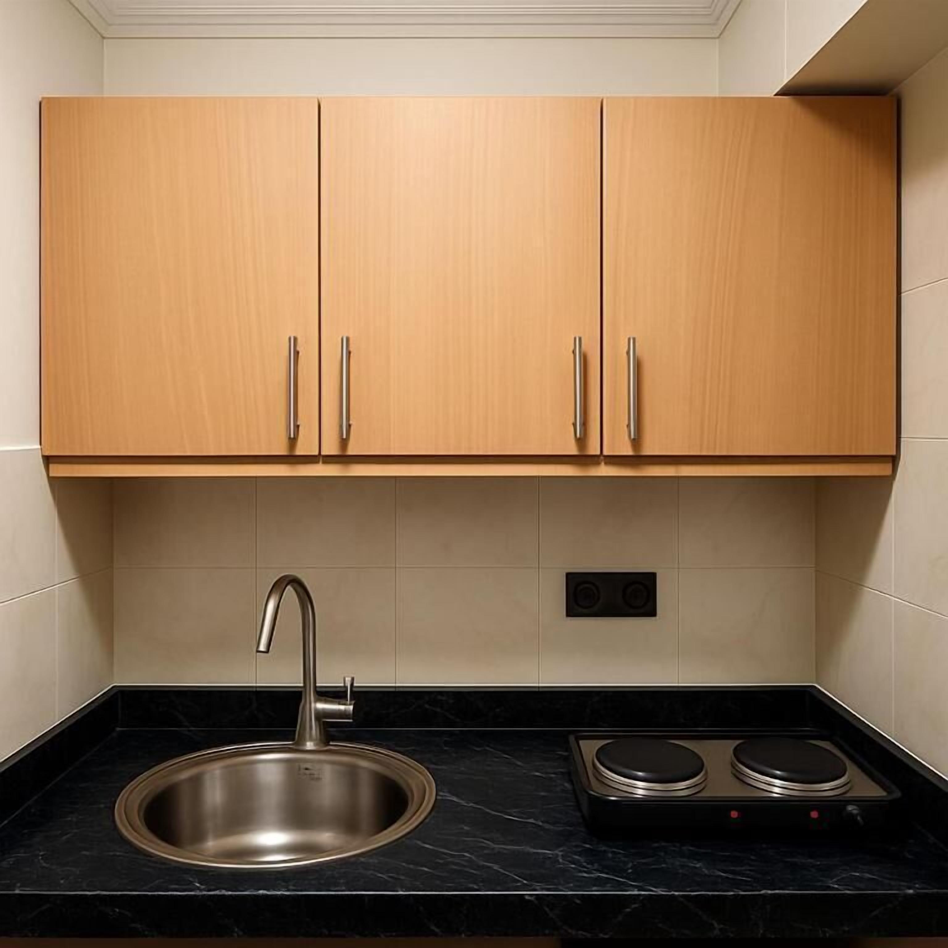 A kitchen with two wooden cabinets, a stainless steel sink, a black countertop, and a built-in stove.