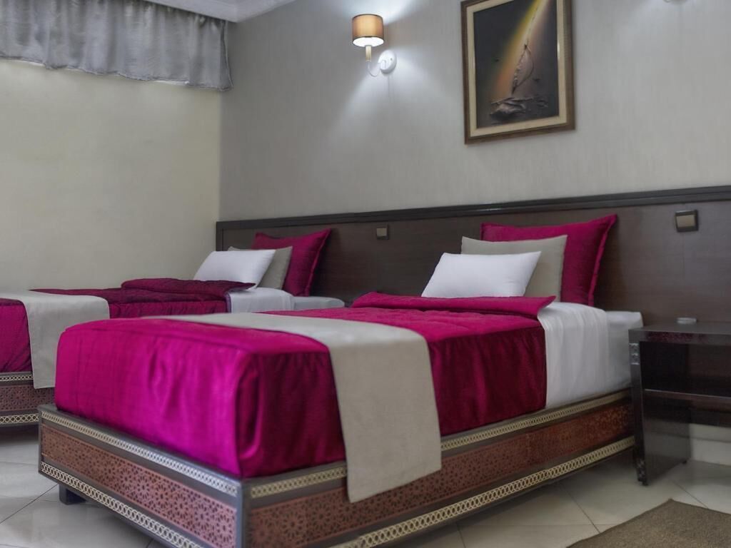 A hotel room with a large bed, a bedside table, and a wall-mounted lamp.