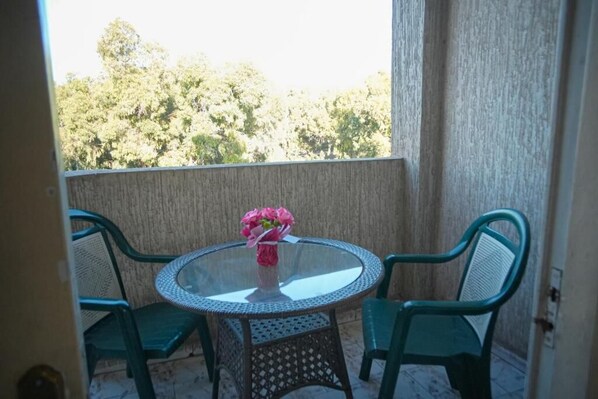A balcony with a round glass table and two chairs, a vase with flowers, and a view of trees. - Isni appart hotel (Agadir)