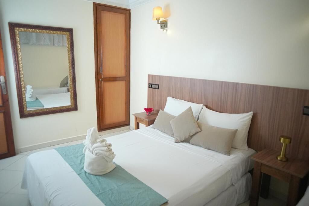 A hotel room with a bed, a nightstand, a wall-mounted lamp, a mirror, and a door.