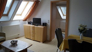 Ein Zimmer mit Schreibtisch, Stuhl, Schrank mit Flachbildfernseher, Heizkörper und Dachfenstern.