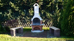 A brick outdoor oven with a white chimney, surrounded by a wooden fence and greenery. - Wittow Apartment for 2 Guests (50 m²) in Wiek on Rügen (Wiek)