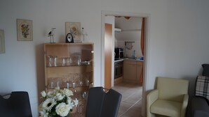 A living room with a glass-top dining table, a sofa, and a chair. There is a kitchen visible through an open doorway. - Wittow Apartment for 2 Guests (50 m²) in Wiek on Rügen (Wiek)