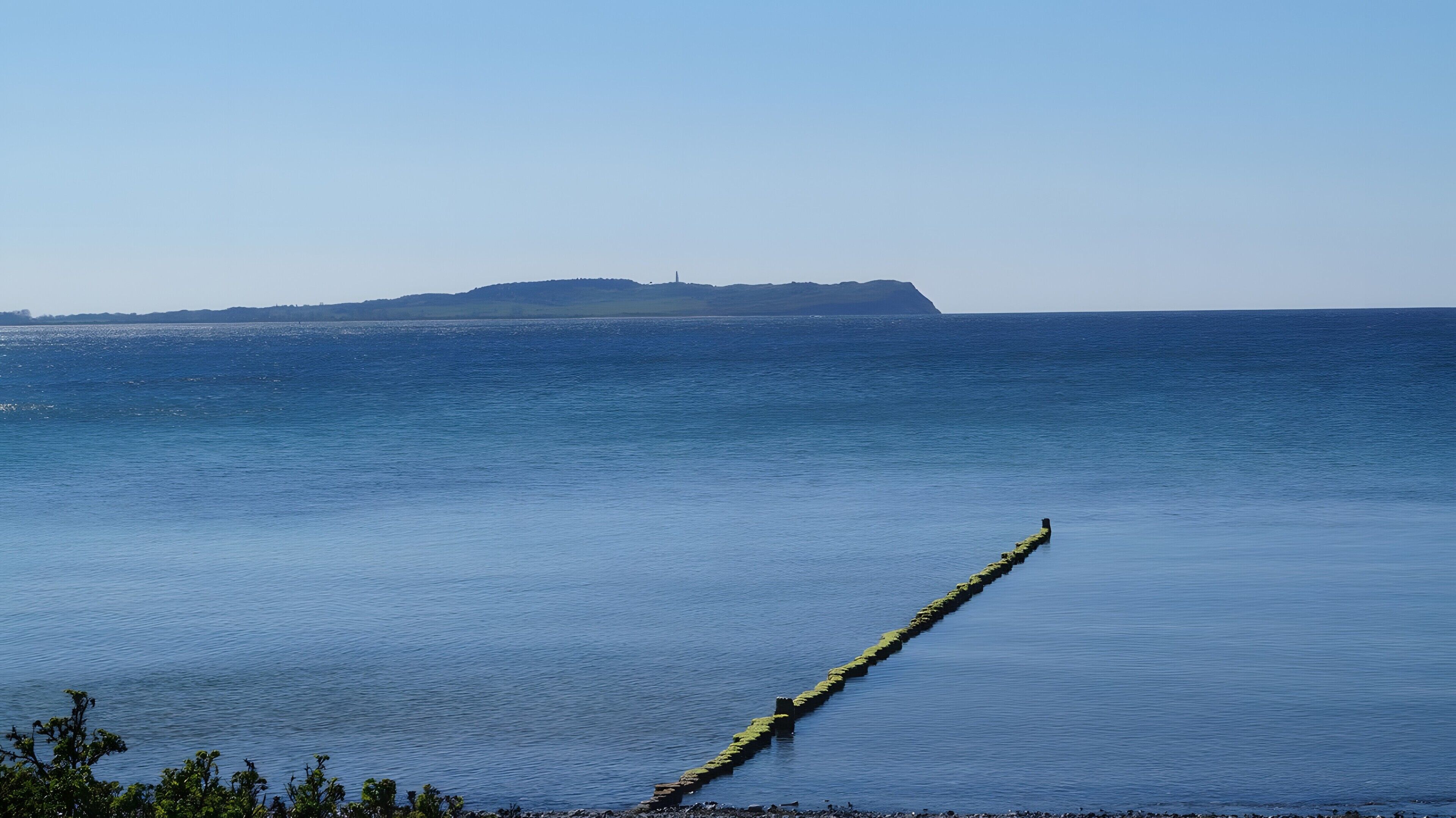 Une mer calme, avec une île lointaine et une longue digue étroite qui s’avance dans l’eau.
