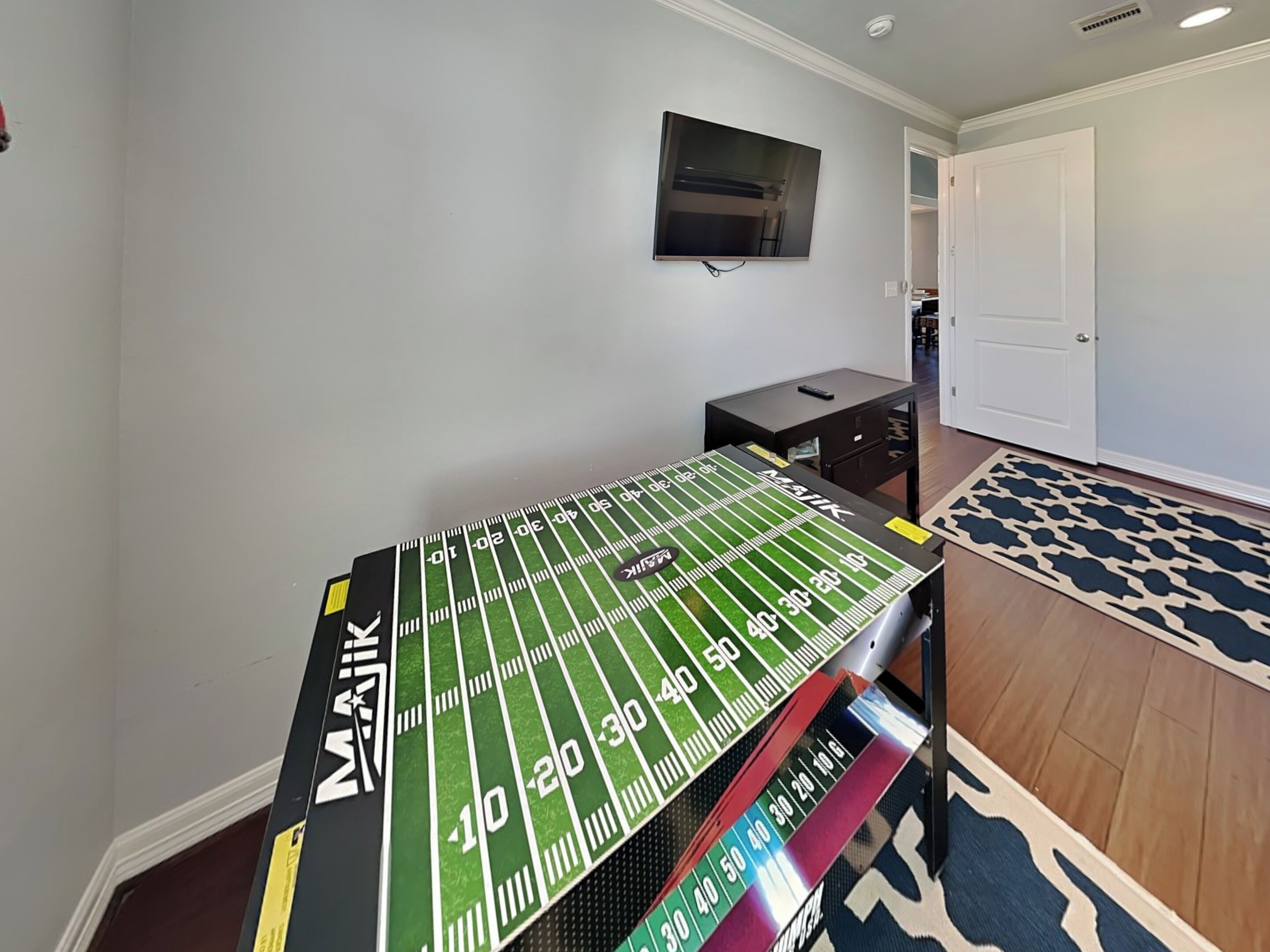 Une pièce avec une table de baby-foot, un téléviseur fixé au mur et un tapis à motifs.