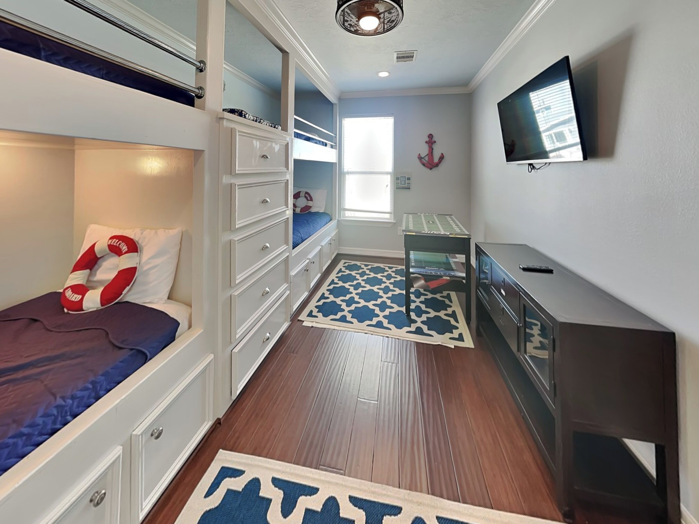 A compact room with bunk beds, a desk, a chair, a television, and a patterned rug.