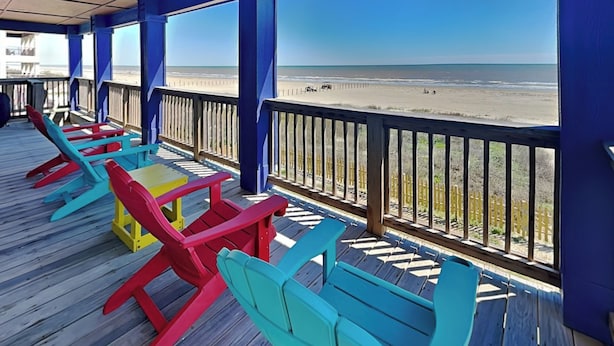 Varanda coberta com cadeiras Adirondack coloridas e vista para a praia.