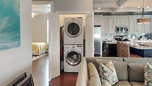 Uma sala de estar moderna com sofá, máquina de lavar e cozinha com armários e micro-ondas.