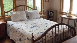 Una camera da letto con un letto in legno, un comodino, un tavolino e una finestra che si affaccia su alberi.