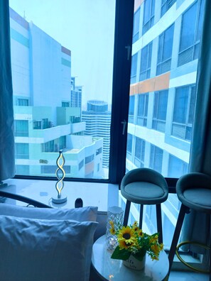 A hotel room with a large window, a bed, two chairs, a table with a vase of flowers, and a decorative item. - Ideal Family Getaway Connected to Eastwood Mall (Metro Manila, Quezon City)