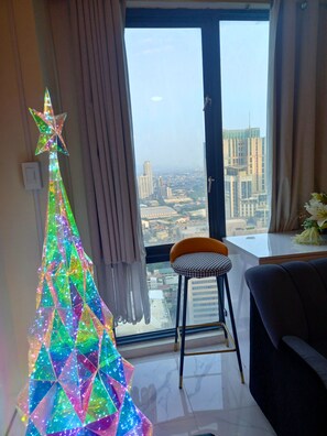 A modern living room with a large window, a colorful star-shaped decoration, a black sofa, and a small stool. - Ideal Family Getaway Connected to Eastwood Mall (Metro Manila, Quezon City)