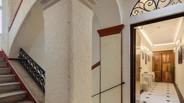 A staircase with a handrail, a door with a handle, and a hallway leading to a room with a chandelier. - Retreat Inside Diocletian's Palace (Split)
