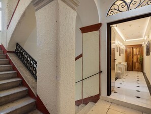 Eine Treppe mit Handlauf, eine Tür mit Griff und ein Gang, der zu einem Raum mit einem Chandelier führt.