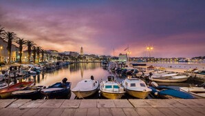 A marina with boats docked, a calm water body, and a cityscape with buildings in the background. - Retreat Inside Diocletian's Palace (Split)