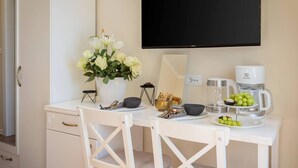 A hotel room with a white desk, a flat-screen TV, a coffee maker, a bowl of fruit, and a vase of flowers. - Retreat Inside Diocletian's Palace (Split)