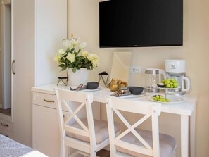 A hotel room with a white desk, a flat-screen TV, a coffee maker, a bowl of fruit, and a vase of flowers. - Retreat Inside Diocletian's Palace (Split)