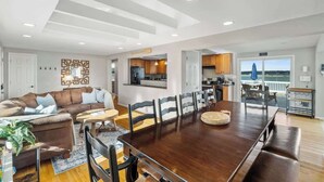 A spacious living room with a large wooden dining table, a cozy seating area, and a view of the ocean.