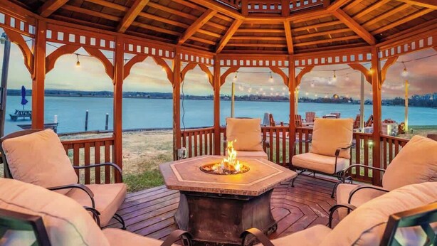 A wooden gazebo with a fire pit, outdoor seating, and a view of the water.
