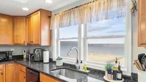 A kitchen with wooden cabinets, a granite countertop, a sink, and a window with a view of the beach.