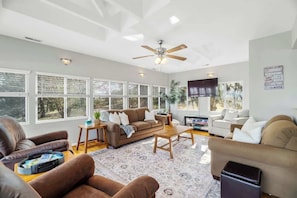 A spacious living room with a ceiling fan, large windows, and a flat-screen TV.
