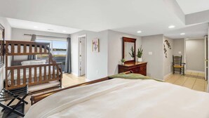 A bedroom with a bunk bed, a desk, a chair, a mirror, and a view of the outdoors.