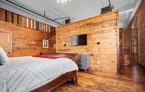 A bedroom with a wooden wall, a bed, a dresser, and a TV mounted on the wall.